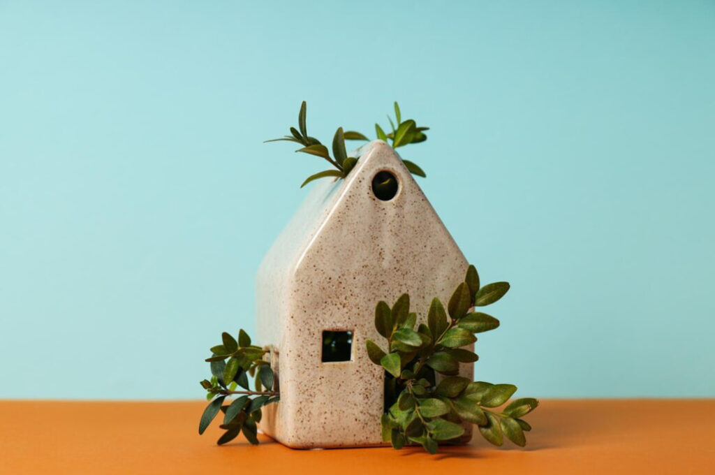 a small white house with plants inside on orange table in the blue background