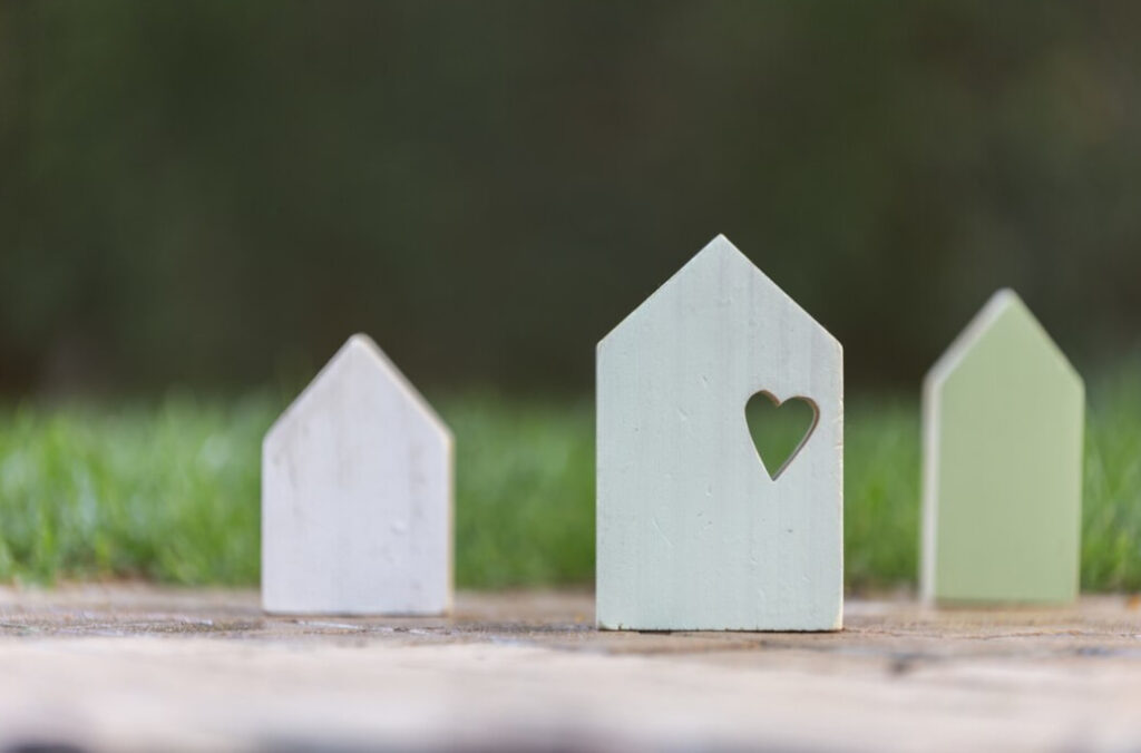 three wooden figures of houses on the lands, the grass behind on a blurred background